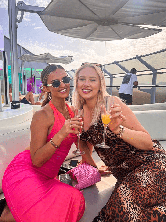 Two women dressed in colorful dresses on a cruise and drinking champagne.