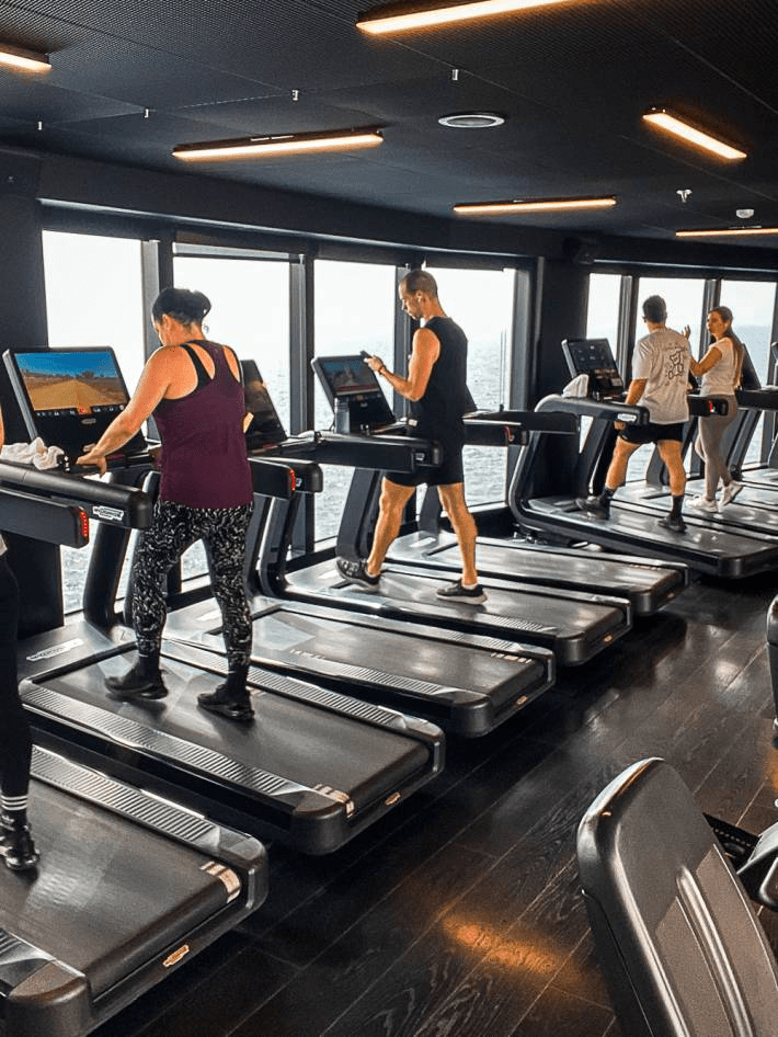 The fitness area of the Virgin Voyages Cruise with people working out.